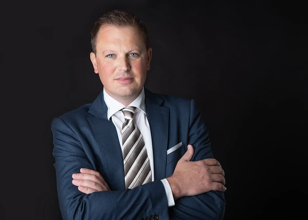 Portrait von Ing. Bernd Hinteregger. Auf schwarzem Hintergrund, stehend, mit Anzug und Krawatte.